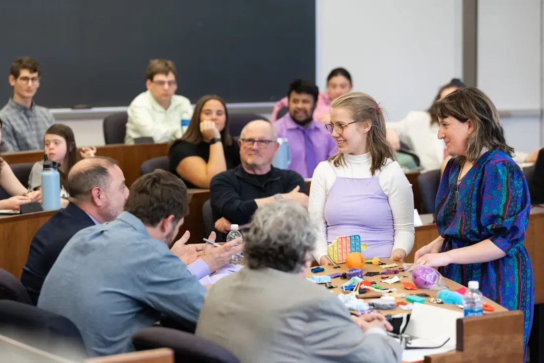 A classroom with two people at the front, teaching a group of people sitting at desks.